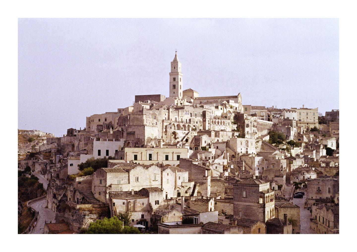 A town with a tall bell tower on a hill is surrounded by many buildings.