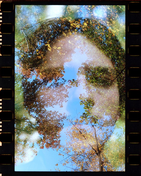 A double exposure shows a woman's face superimposed over a forest with autumn foliage and a blue sky.