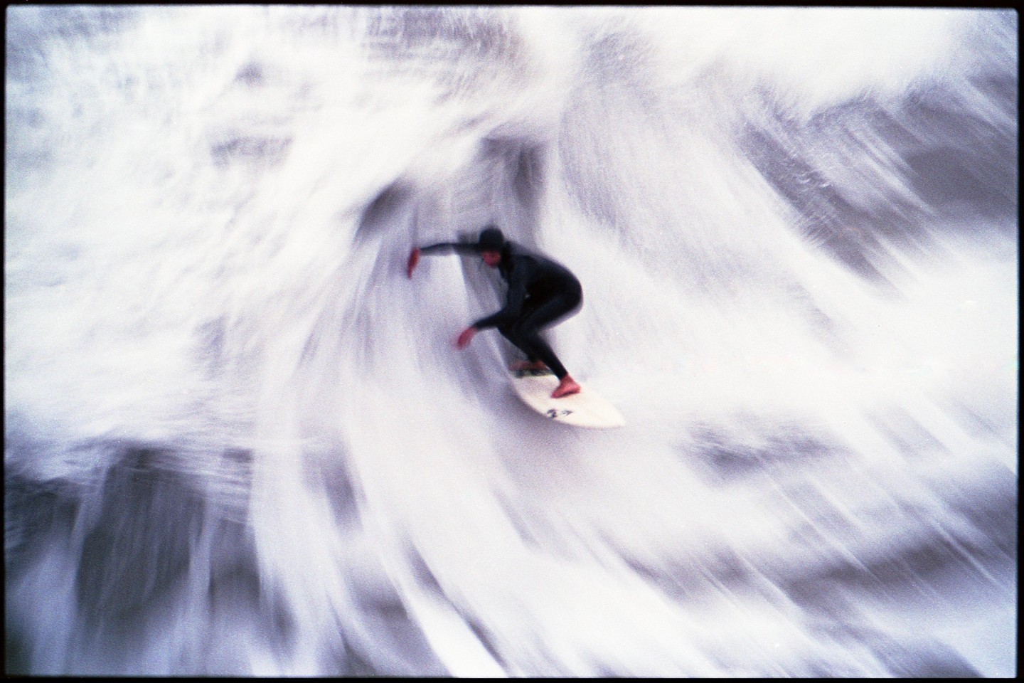 A surfer in a wetsuit rides a wave on a surfboard, with the water blurred around them.