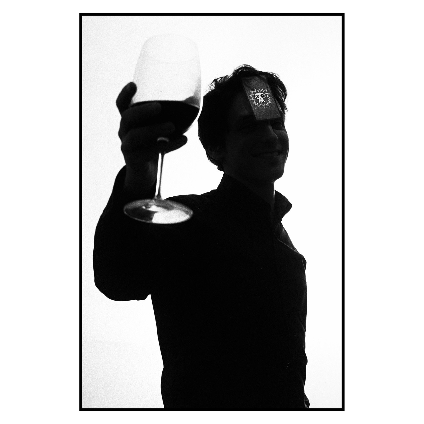 A man holds a wine glass up to the light, with a sticker on his forehead.