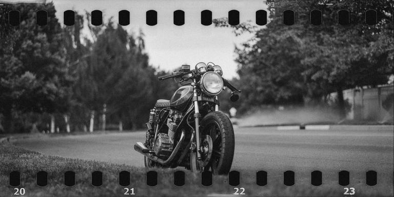 A motorcycle is parked on the grass next to a road lined with trees.