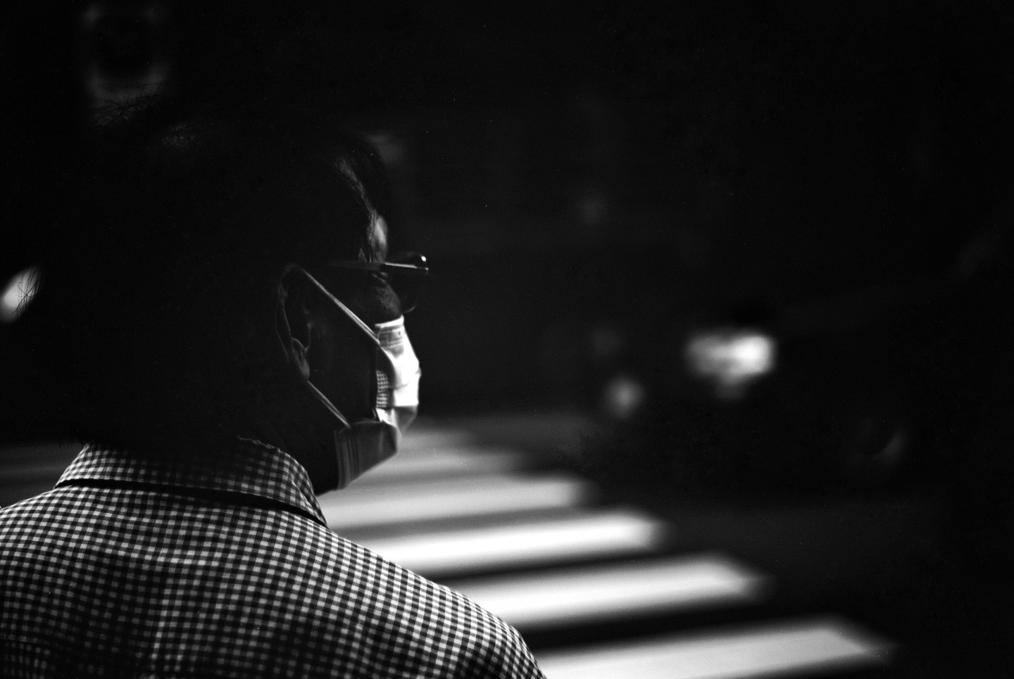 A man wearing a face mask and glasses stands with his back to the viewer, looking towards a crosswalk at night.