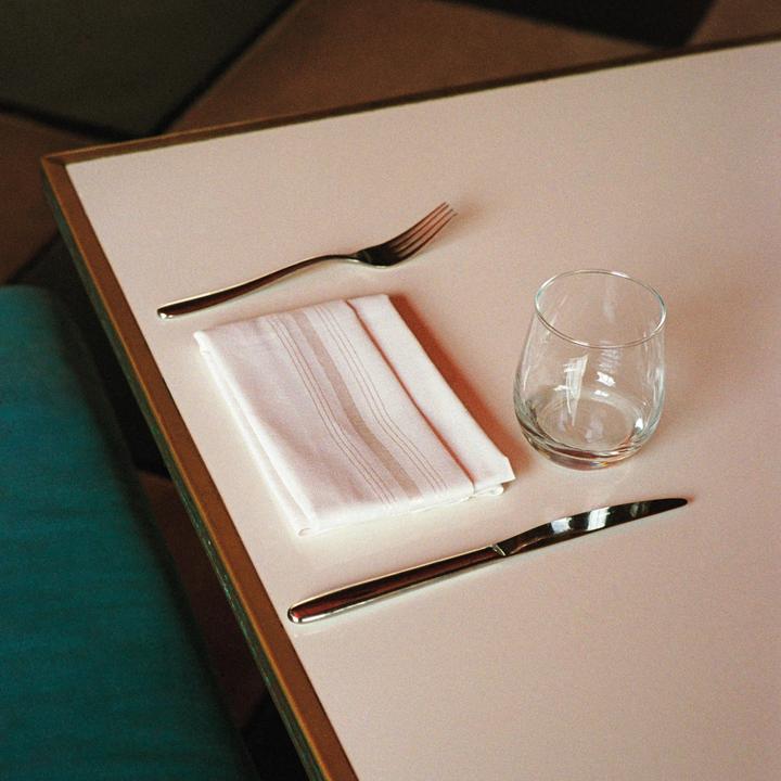 A fork, napkin, glass, and knife are arranged on a table.