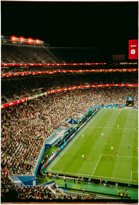 A soccer match is being played on a green field in a stadium filled with spectators at night.