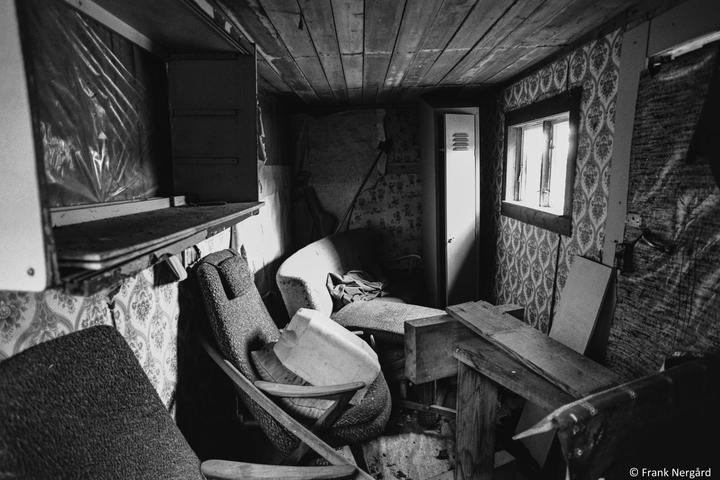 An abandoned room is filled with discarded furniture and debris, illuminated by light from a window.