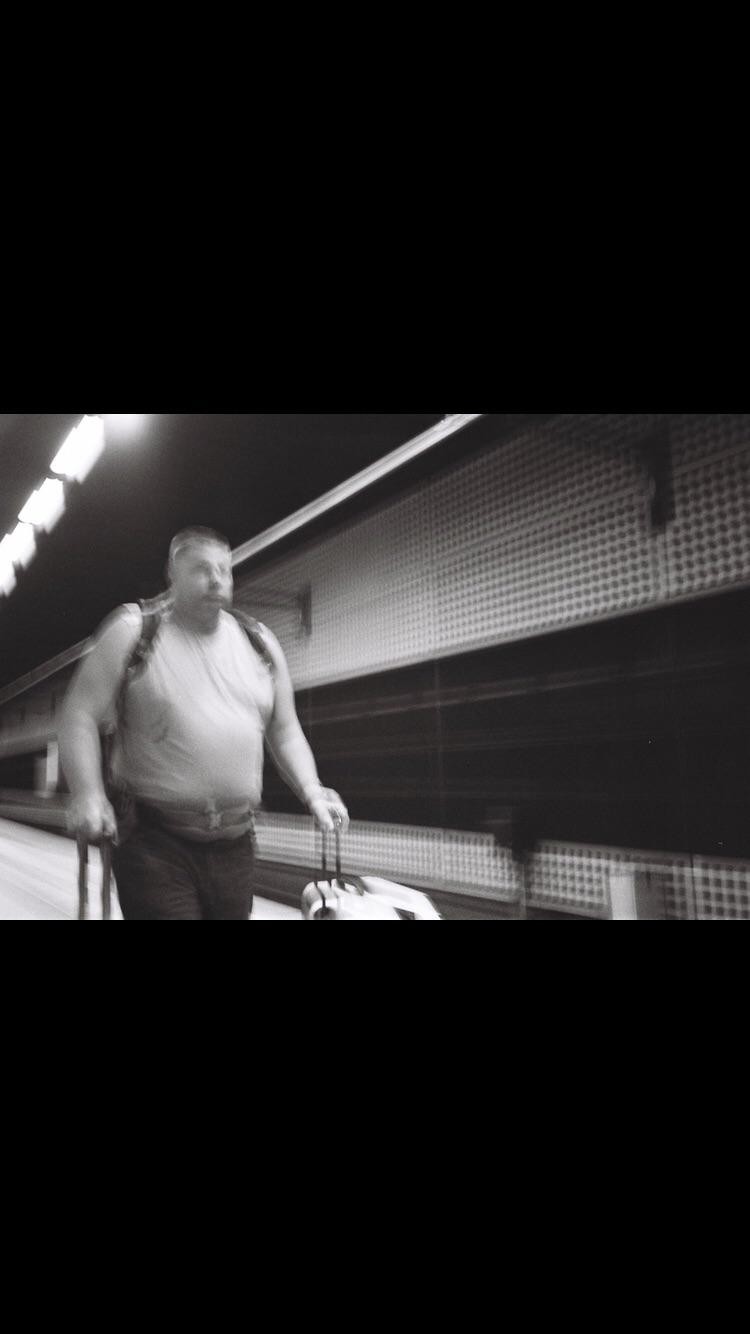 A man with a backpack and rolling luggage walks quickly through a subway station.