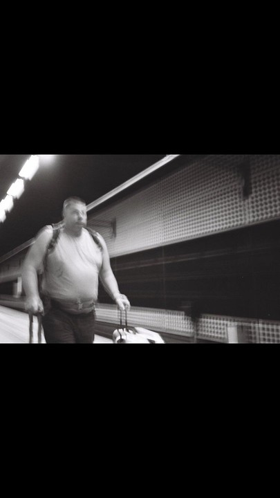 A man with a backpack and rolling luggage walks quickly through a subway station.