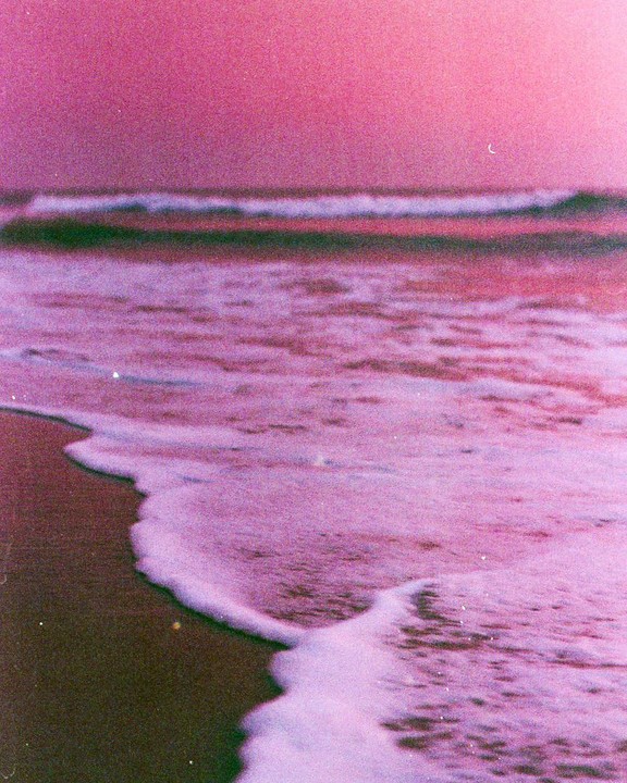 Waves crash on a beach under a pink sky.