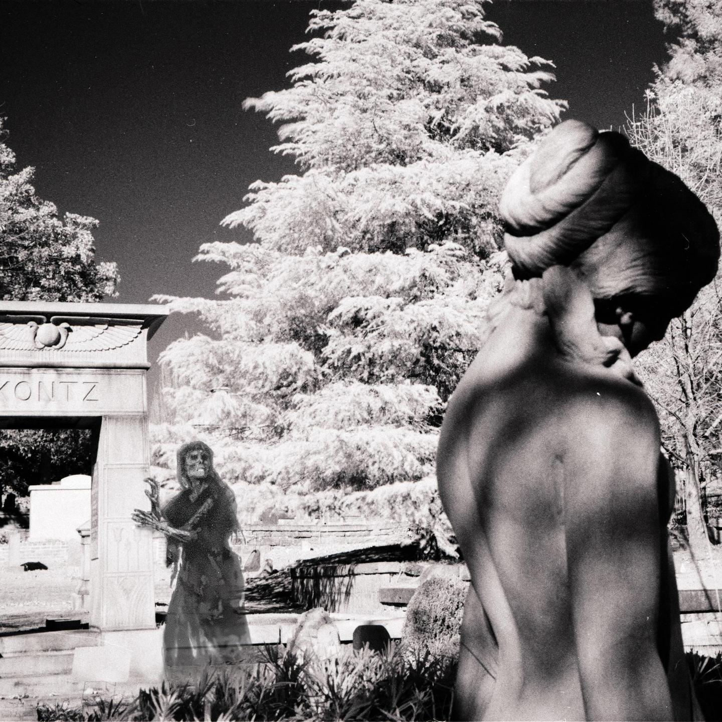 A ghost-like figure stands in front of a tombstone with a statue in the foreground.