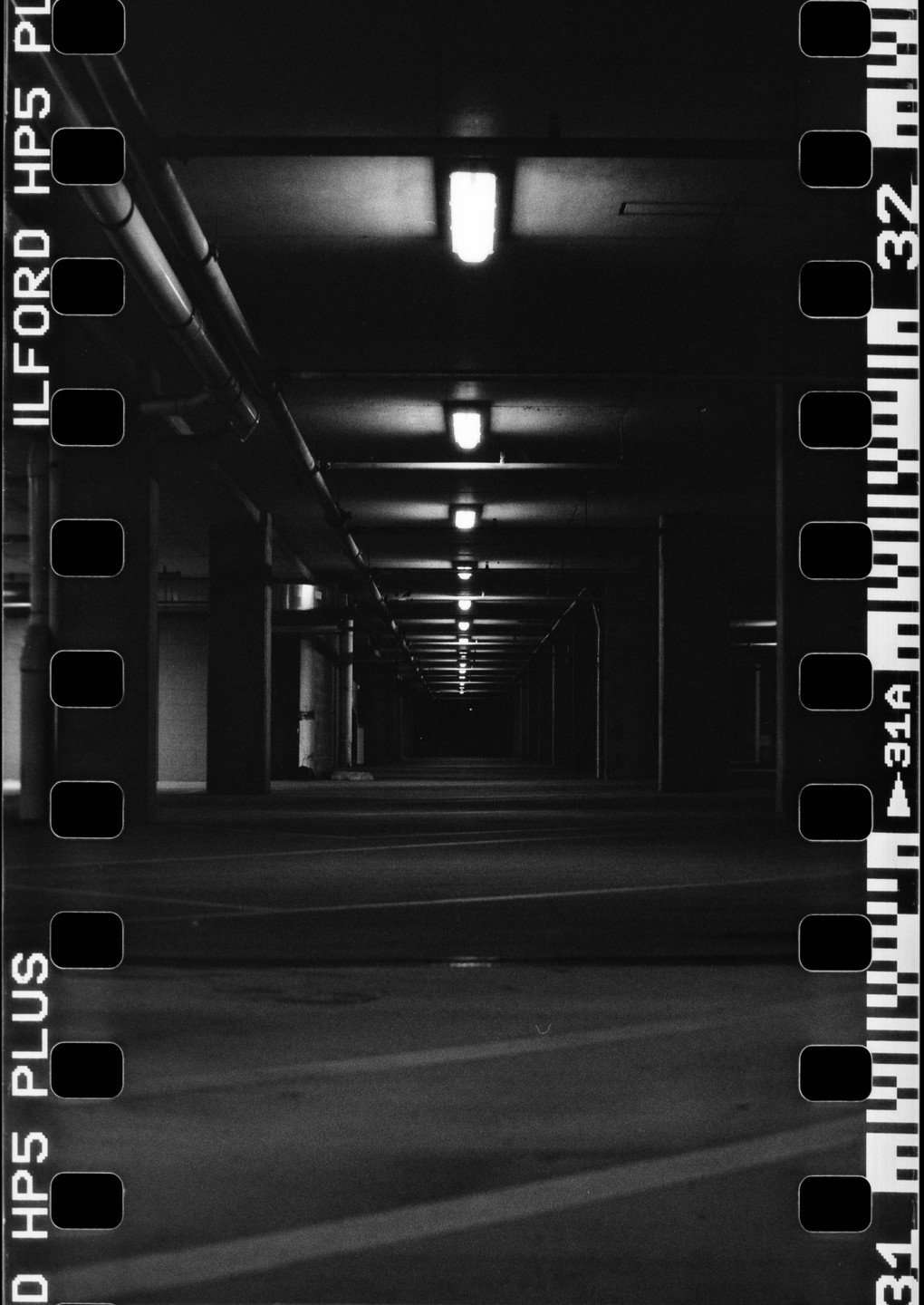 A long, empty parking garage stretches into the distance, illuminated by a row of overhead lights.