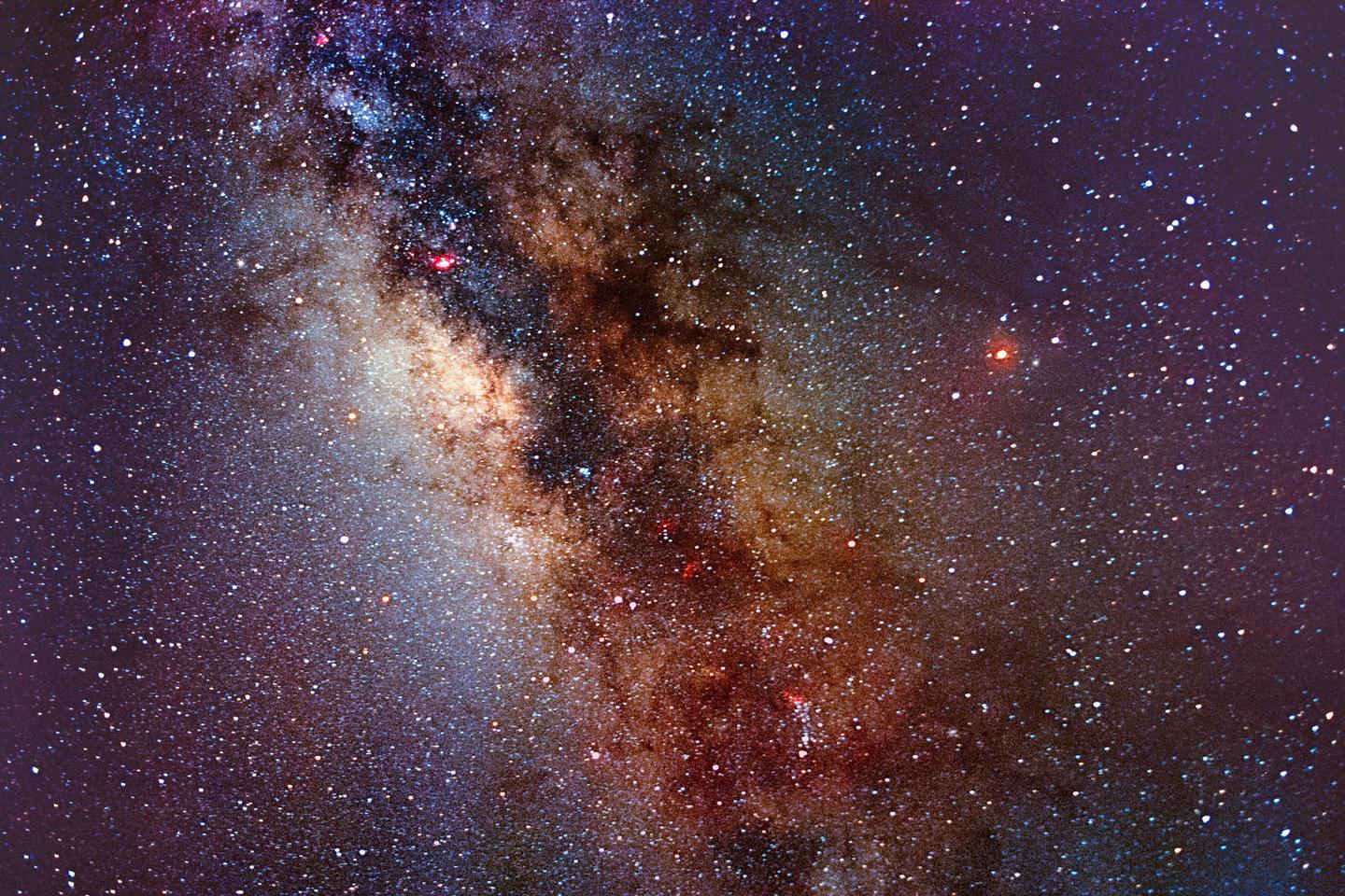 The Milky Way is visible with many stars and some red and blue nebulae.