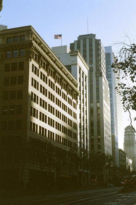 A street is lined with tall buildings, one of which has an American flag flying from its roof.