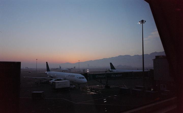 Airplanes are parked on an airport tarmac with mountains in the background at dusk.