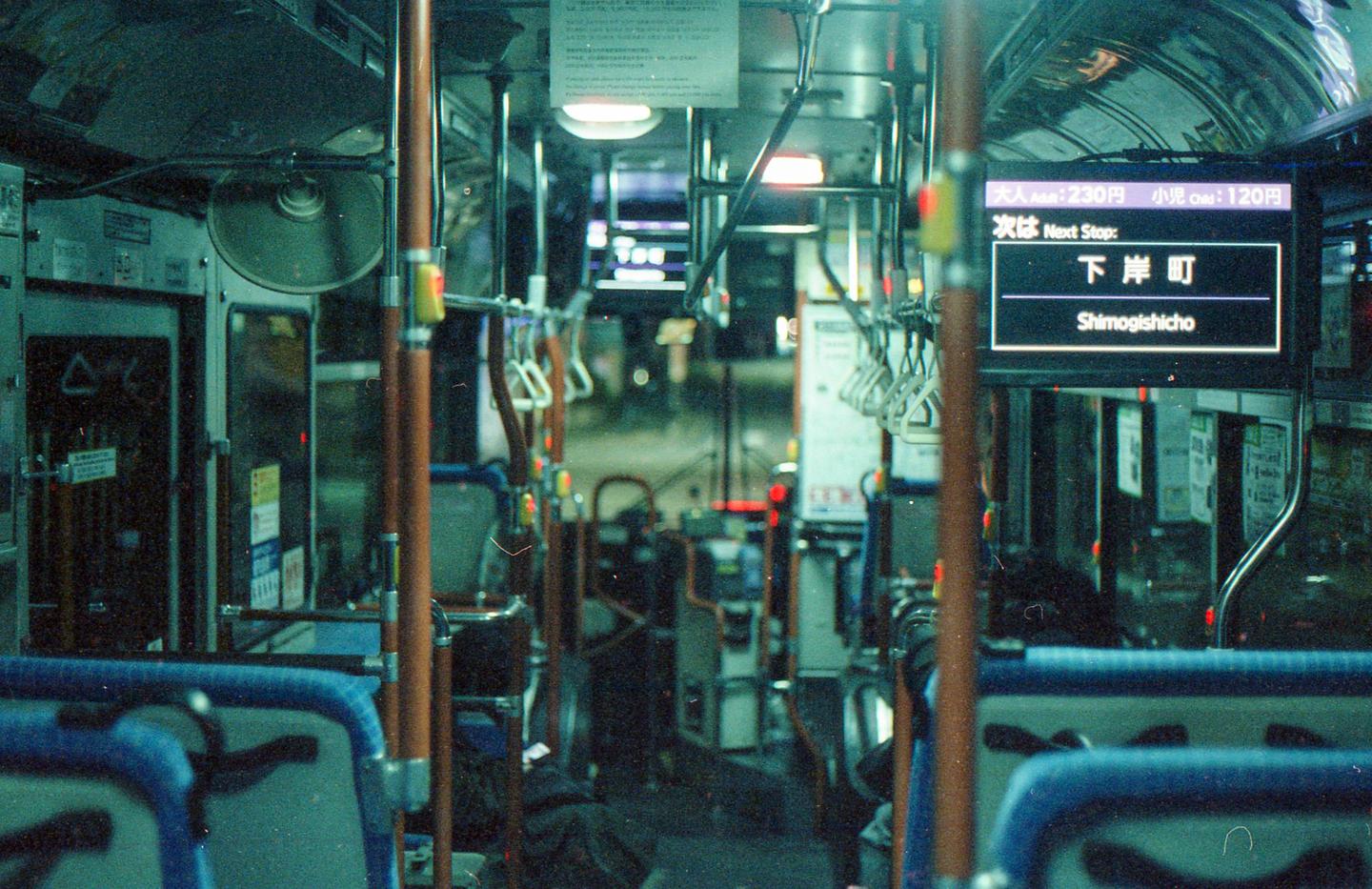 The interior of a bus is visible at night, with blue seats and a digital display showing the next stop.