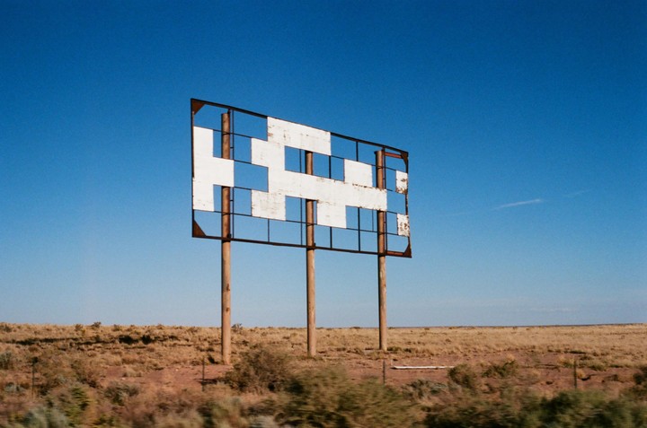A weathered, empty billboard stands in a vast, dry landscape under a clear blue sky.