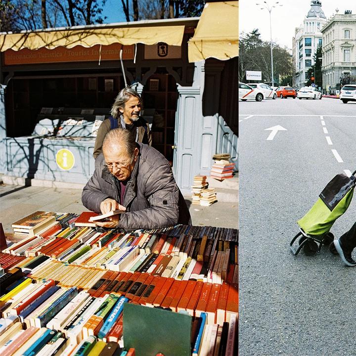 A man in a jacket looks at books on a table in front of a tourist information booth, while another man stands behind him.