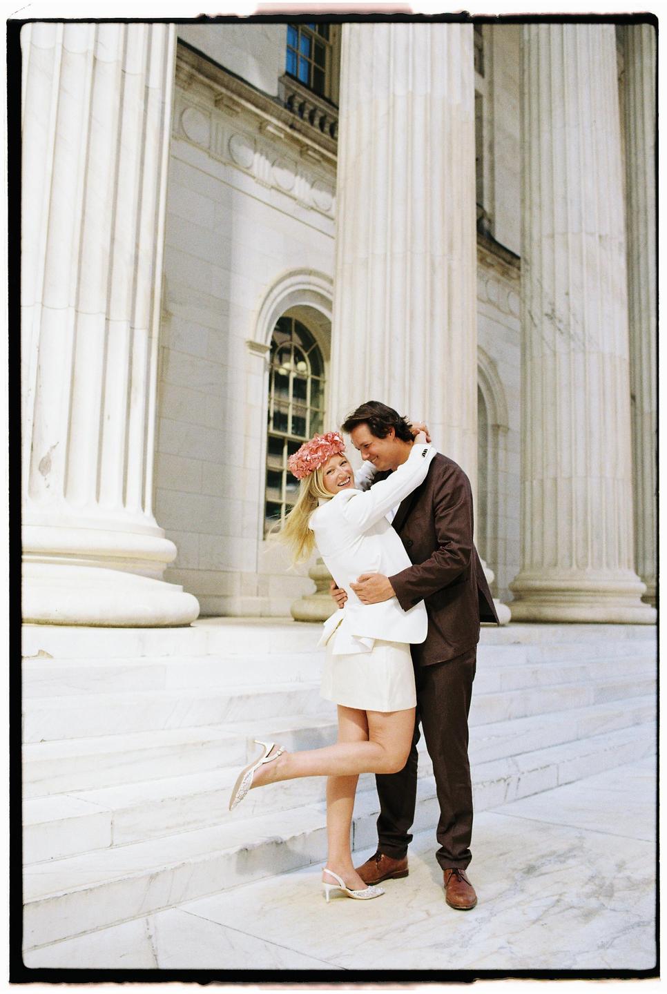 A couple embraces on the steps of a building with large columns.