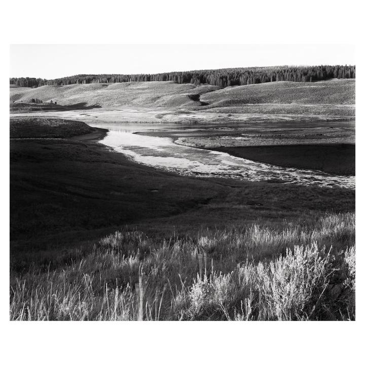 A winding river flows through a valley with hills covered in trees and grass.
