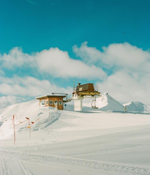 A ski lift and a small wooden building are visible on a snow-covered mountain under a blue sky with clouds.