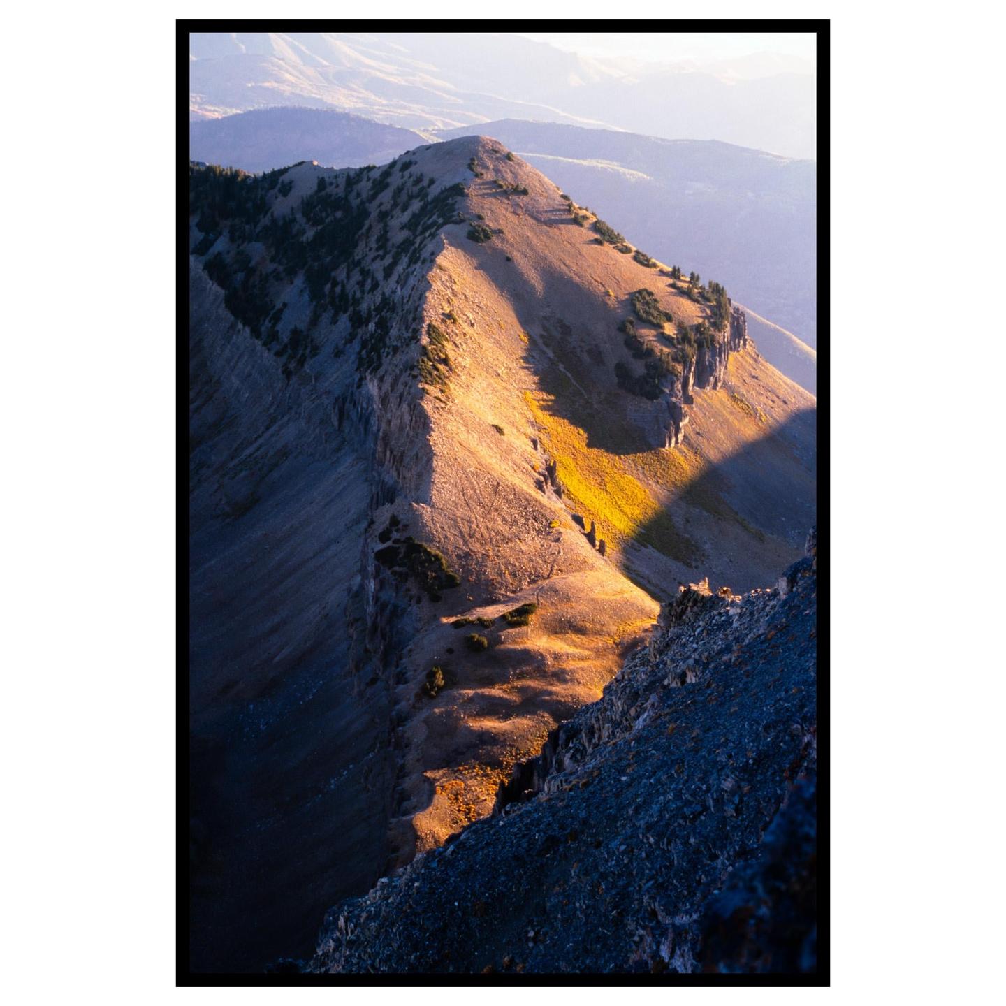A mountain ridge is illuminated by golden light, casting long shadows across the landscape.