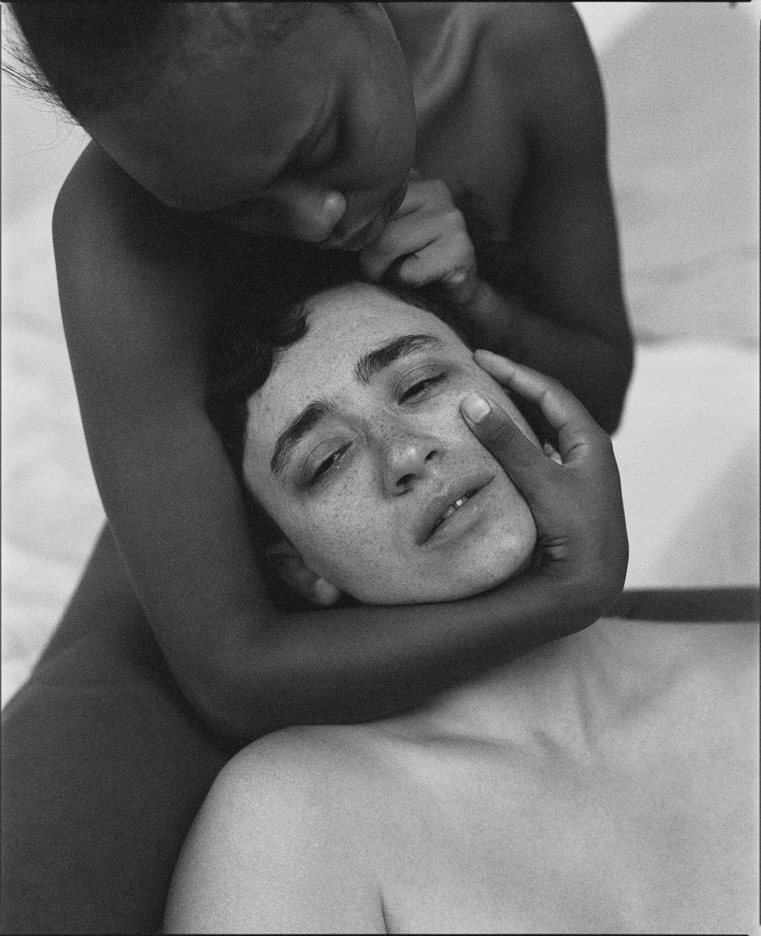 A person with freckles is cradled by another person in a close-up, black and white portrait.