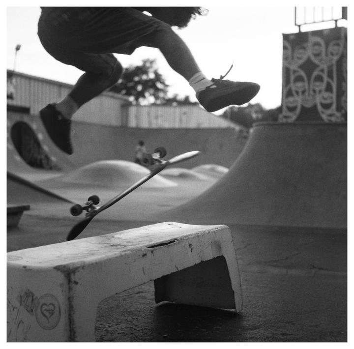 A skateboarder jumps over a concrete bench at a skatepark.