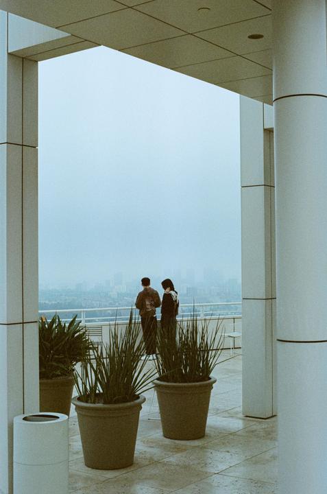 A couple stands on a balcony overlooking a hazy city.