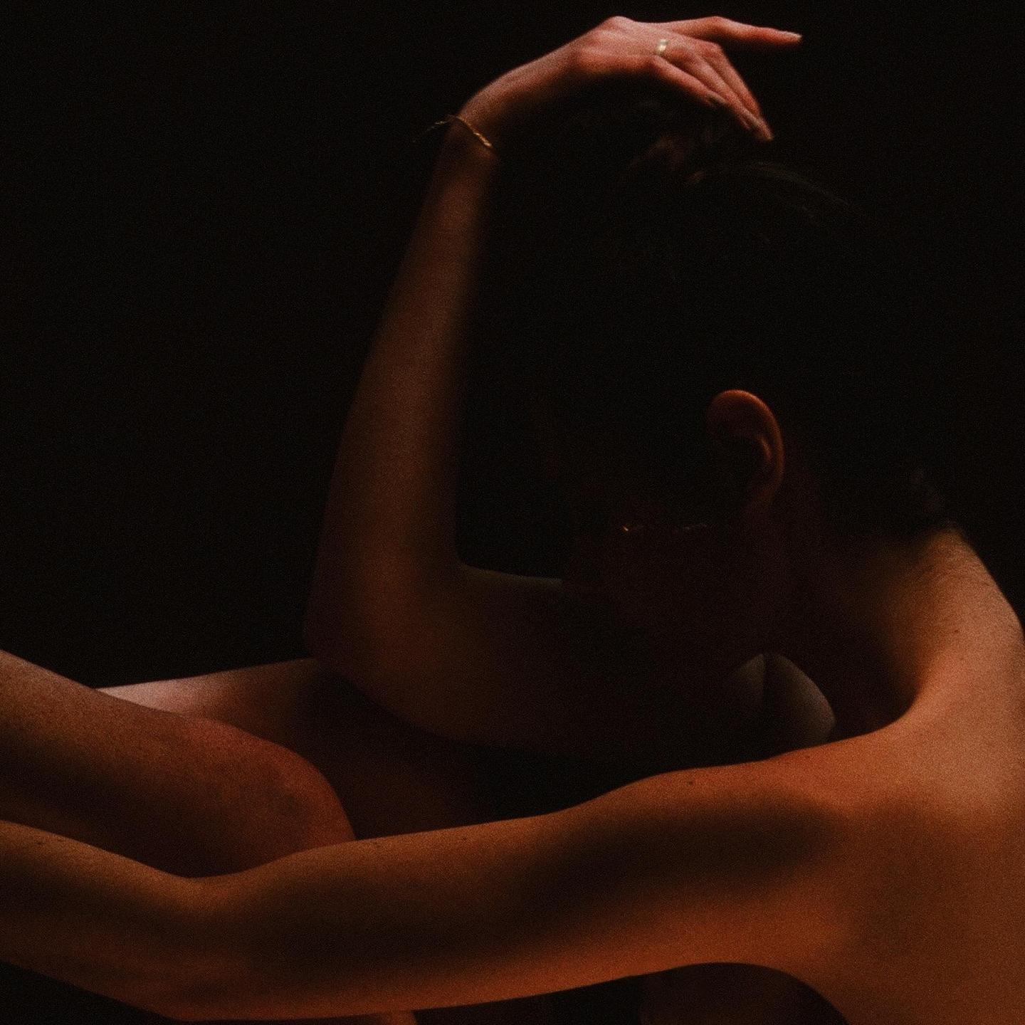 A woman is curled up with her arms around her legs, illuminated by warm light from the side.