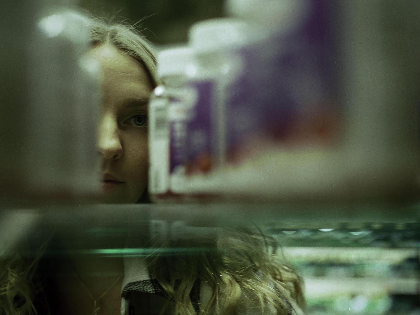 A woman's face is partially visible behind several bottles on a shelf.