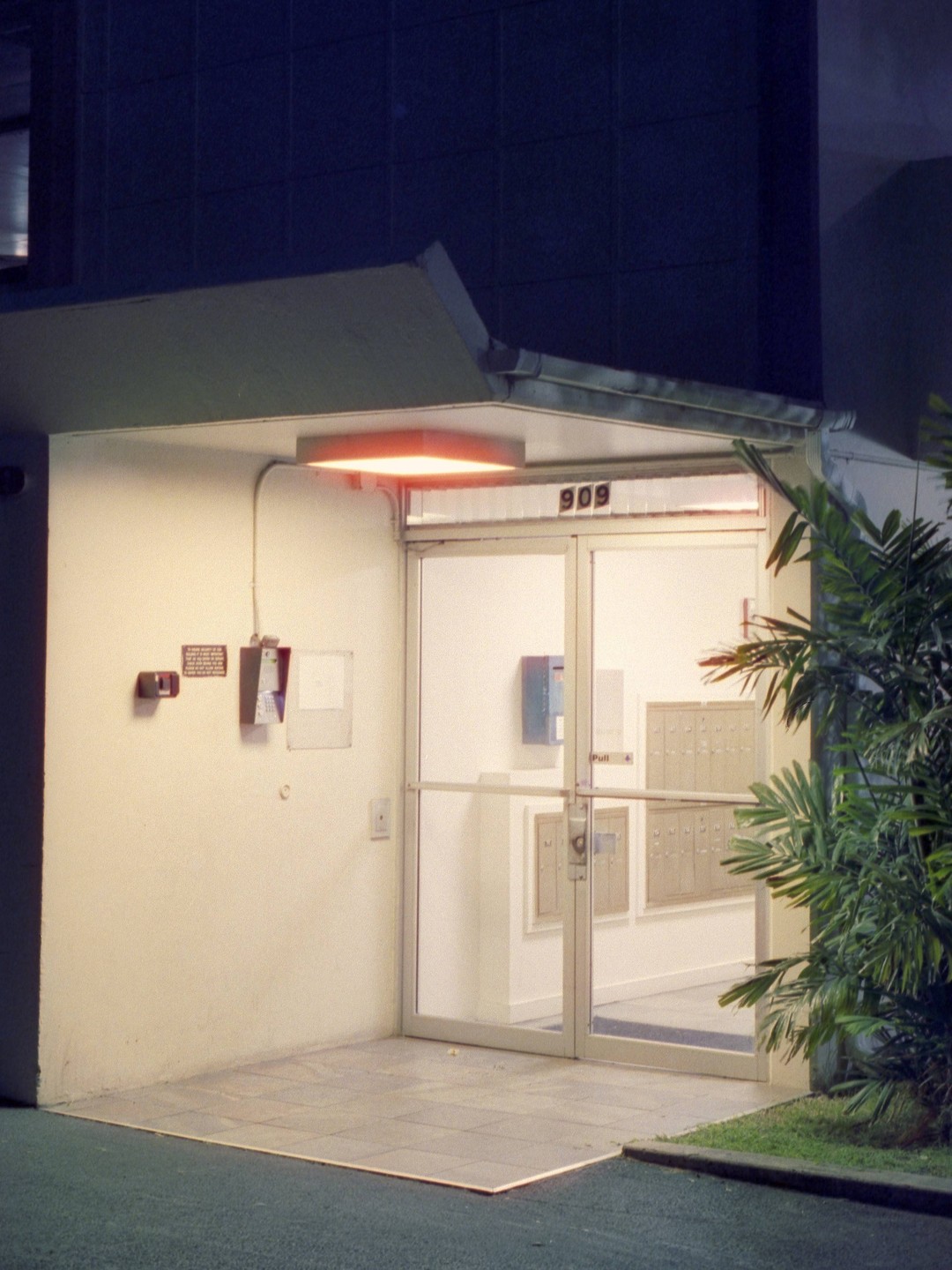 A building entrance with a number 909 above the door is illuminated by an orange light at night.