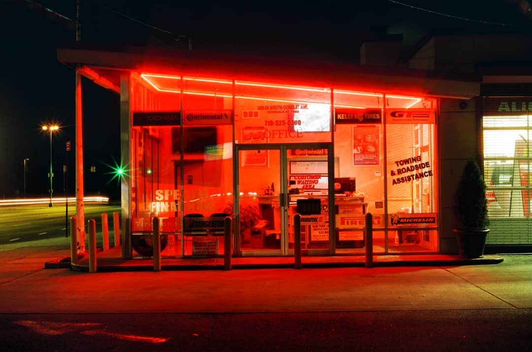 A tire shop with red neon lights illuminates the street at night.