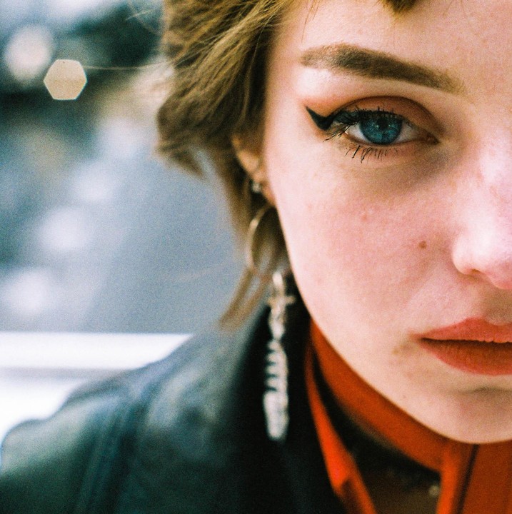 A woman with blue eyes and red lipstick looks directly at the viewer.