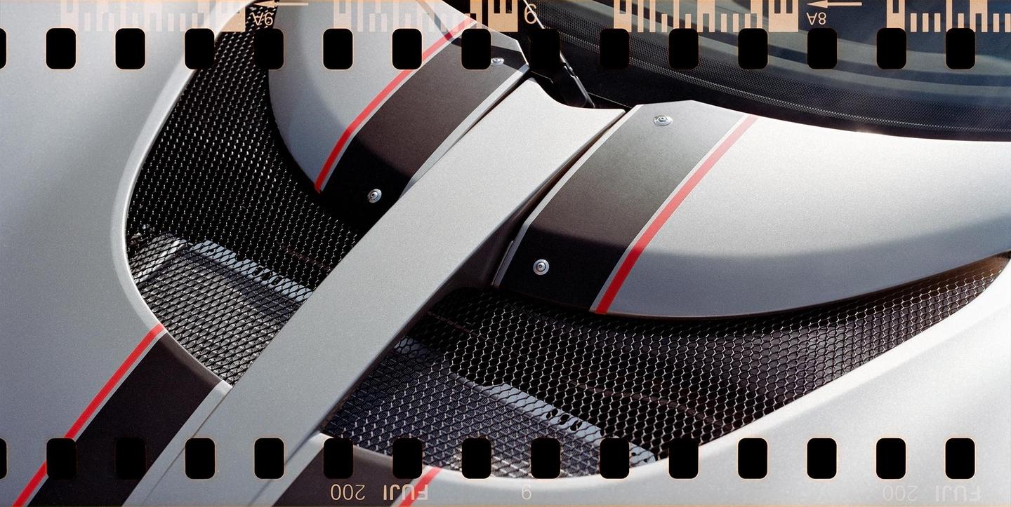 A close-up shot shows the details of a silver car with black and red stripes and a black mesh grill.