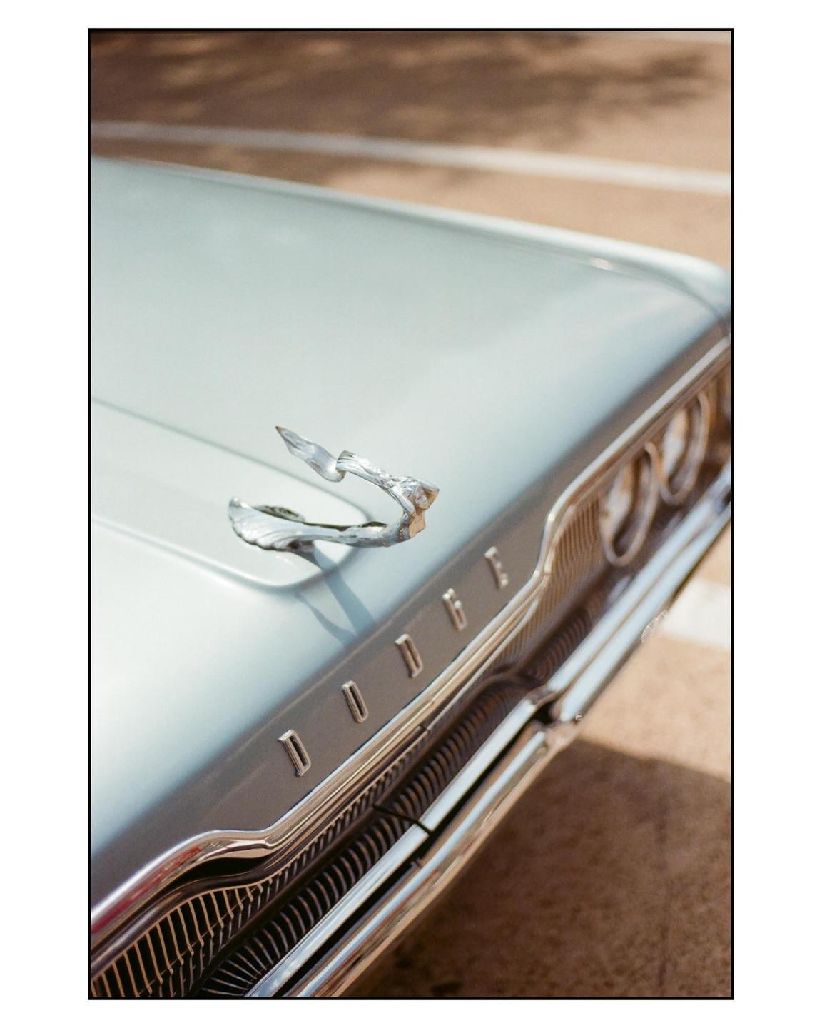 A close-up shot shows the hood ornament and grille of a classic blue Dodge car.