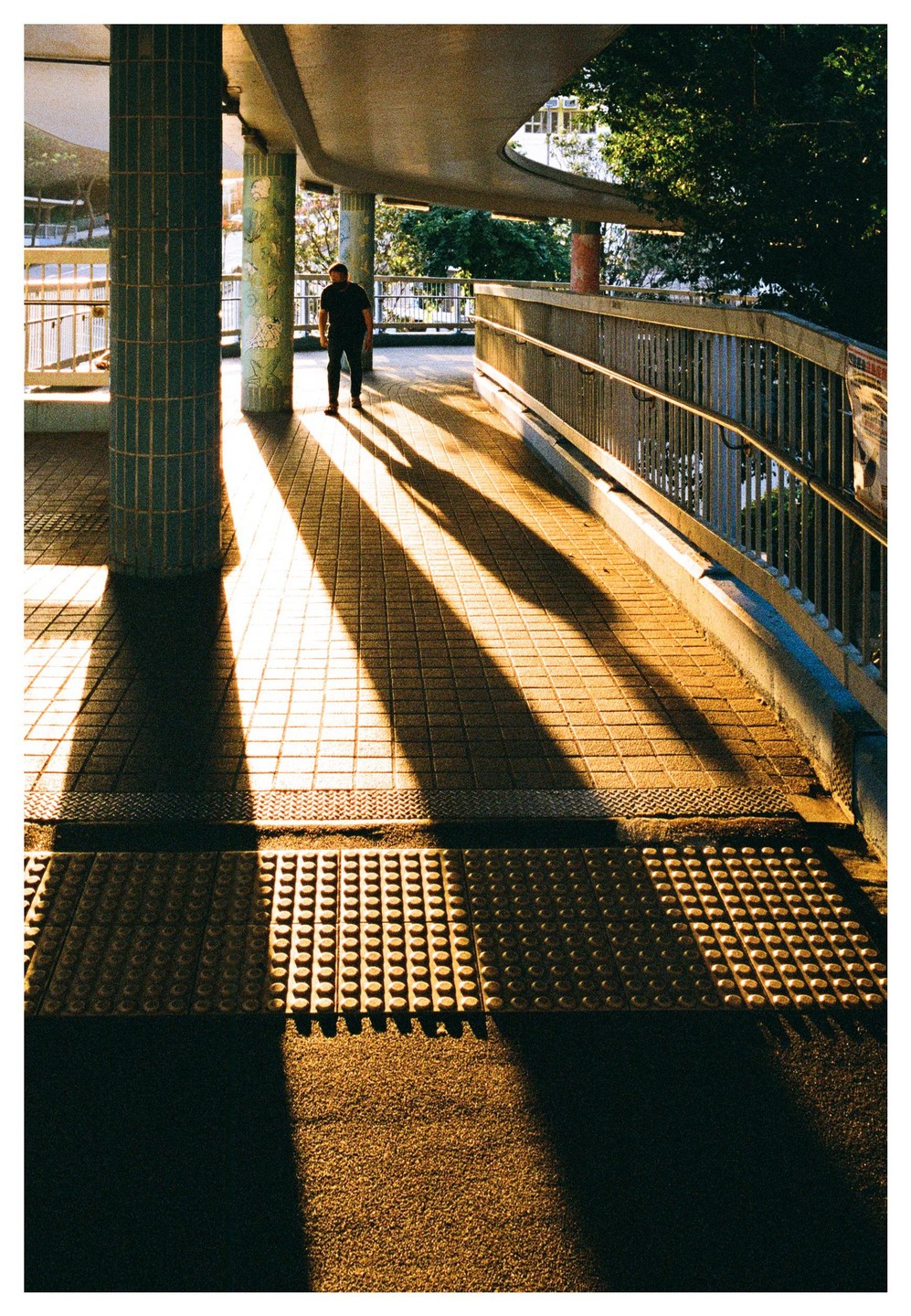 A man walks on a tiled path with long shadows cast by the setting sun.