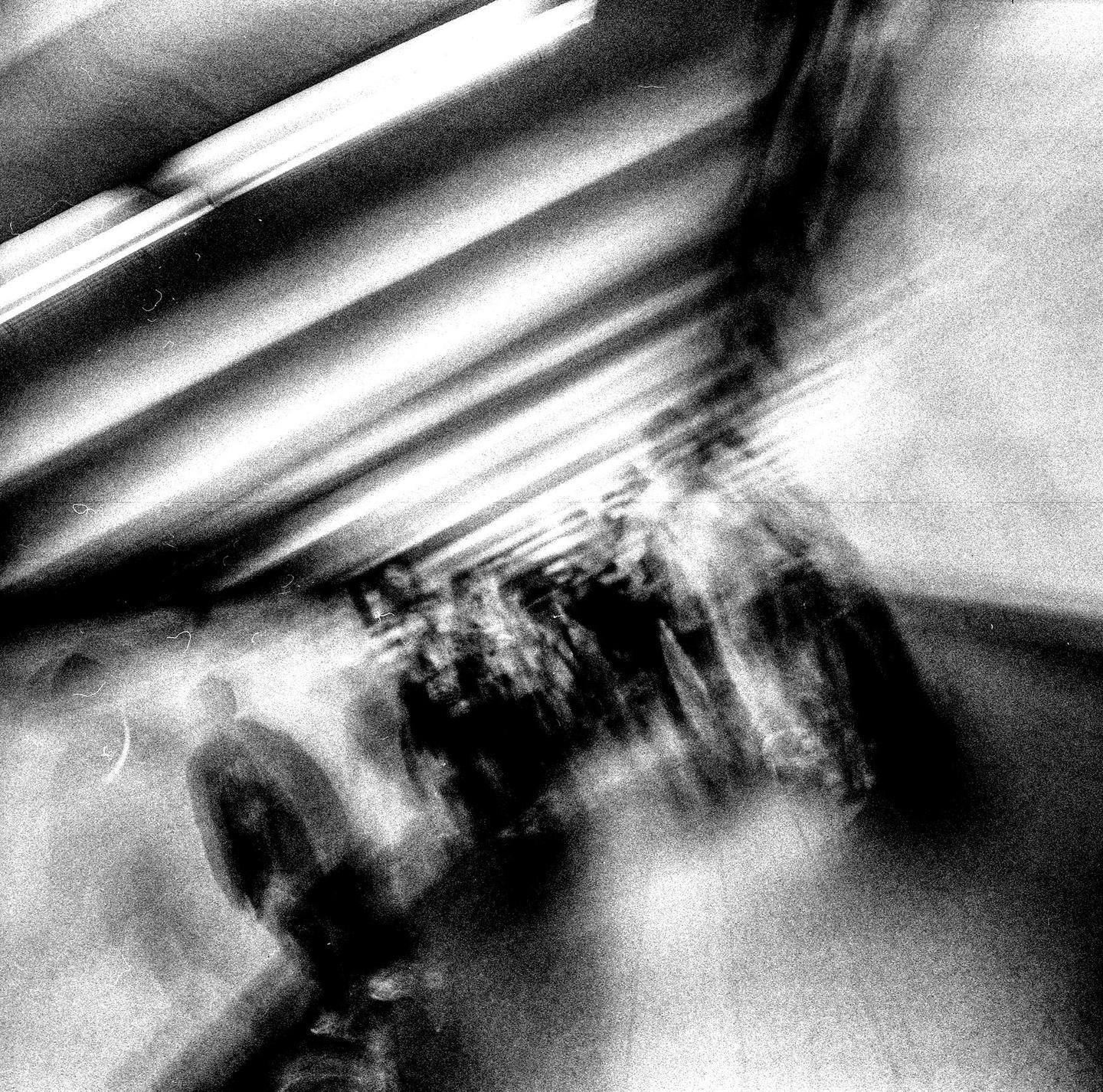 A blurry black and white image shows people walking in a tunnel with bright lights on the ceiling.