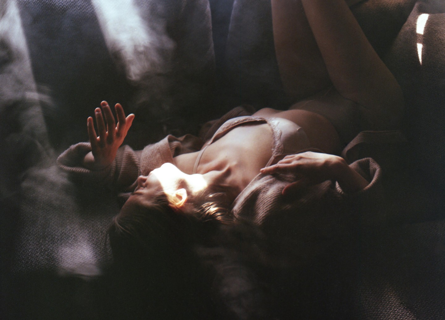 A woman lies on a dark surface with light illuminating her face and hand.