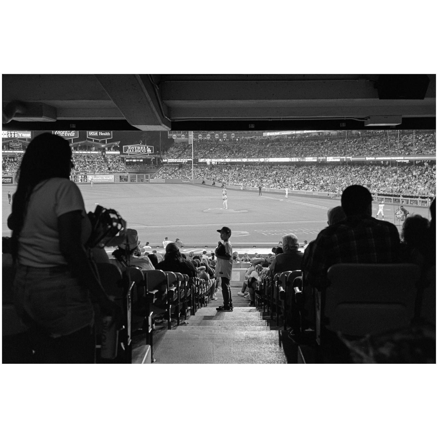 A crowd of people watches a baseball game from the stands of a stadium.