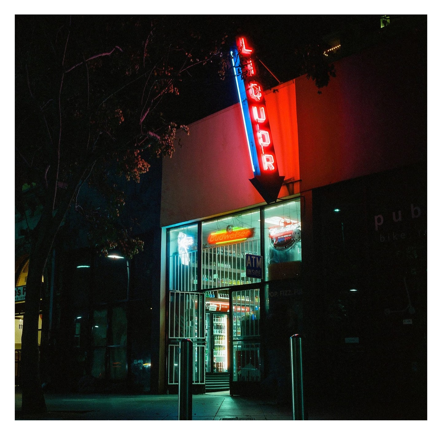 A neon liquor sign with an arrow points down to a store at night.