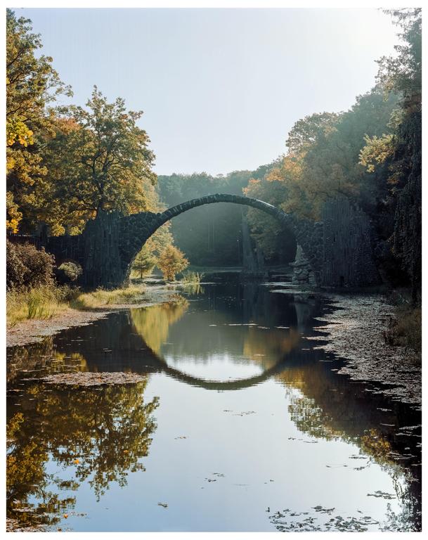 A stone bridge forms a perfect circle with its reflection in the water, surrounded by autumn trees.