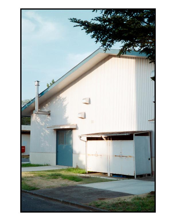 A white building with a blue door and a small shed is seen from a low angle.