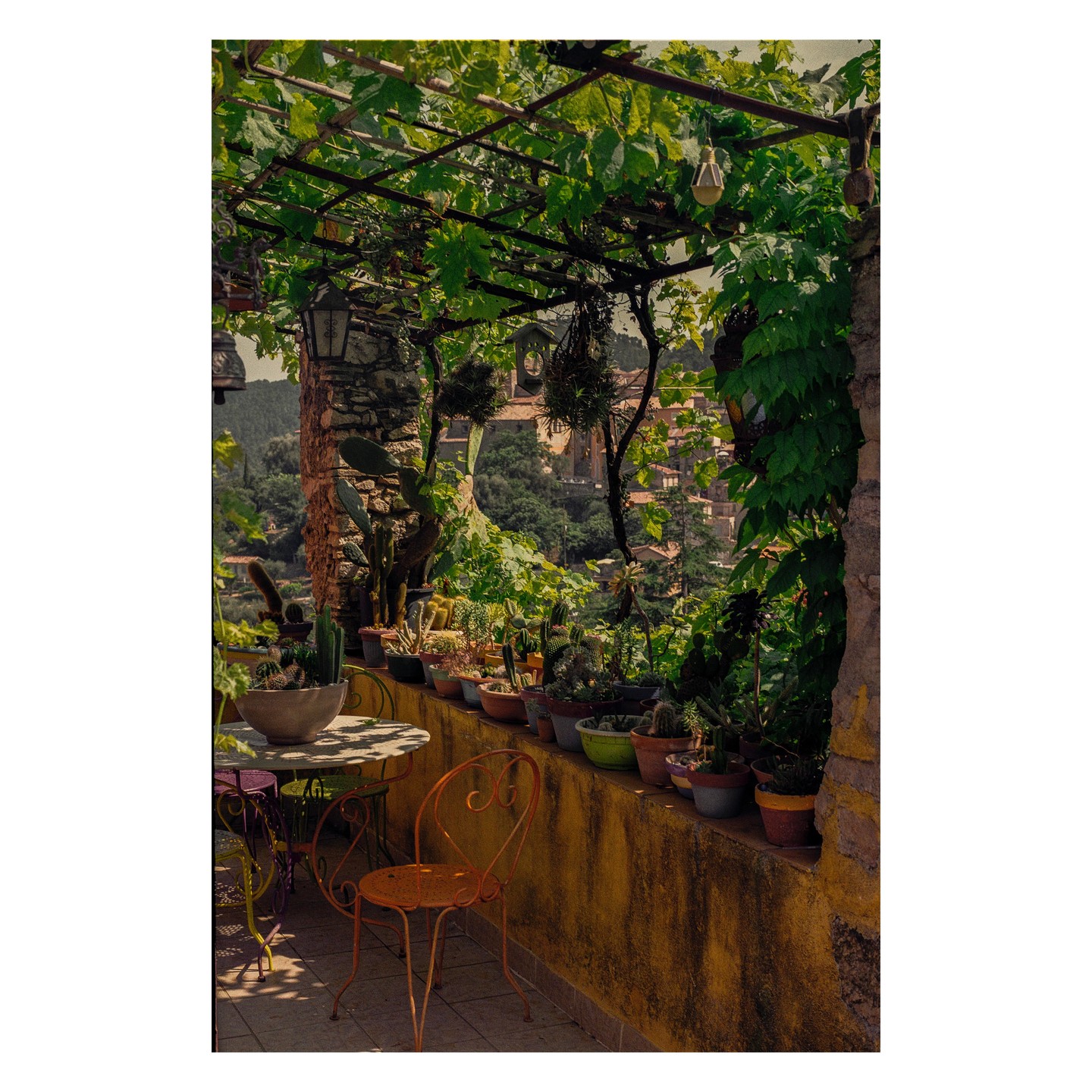 A patio with potted plants and a table and chairs overlooks a village.