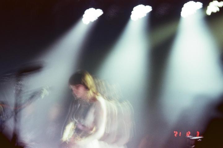 A woman with long hair is playing an instrument on a stage with bright spotlights and haze.