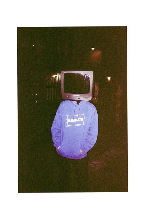 A person wearing a purple Blockbuster hoodie has a television for a head.