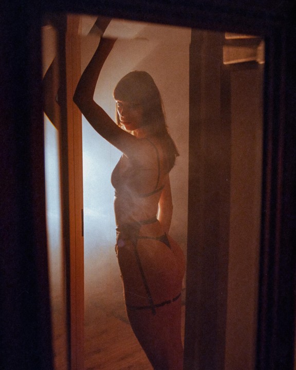 A woman in lingerie poses in a doorway, reflected in a mirror.