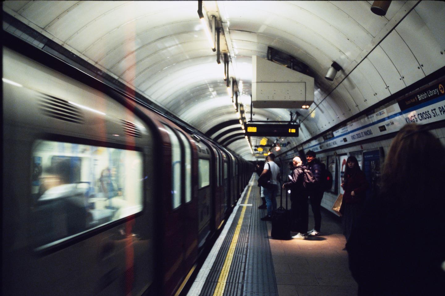 A train pulls into a subway station where people wait on the platform.