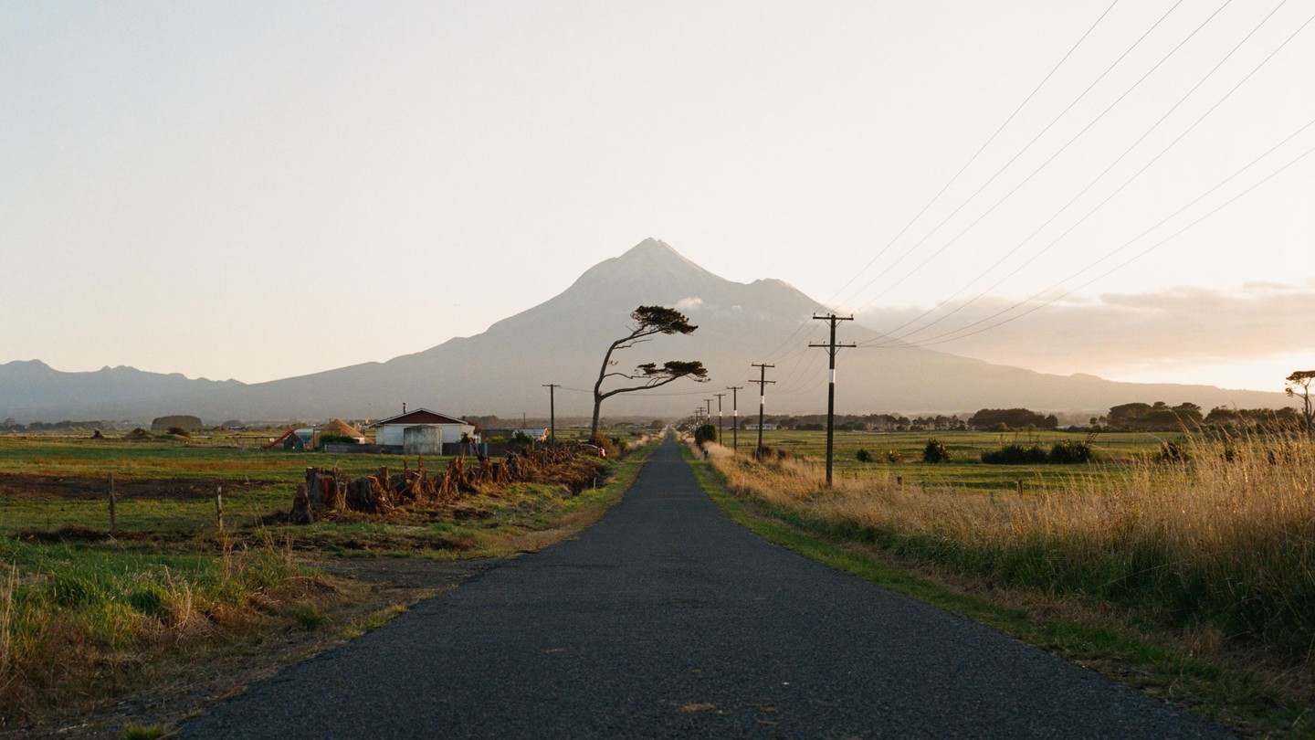 A long, straight road leads towards a large mountain under a hazy sky.