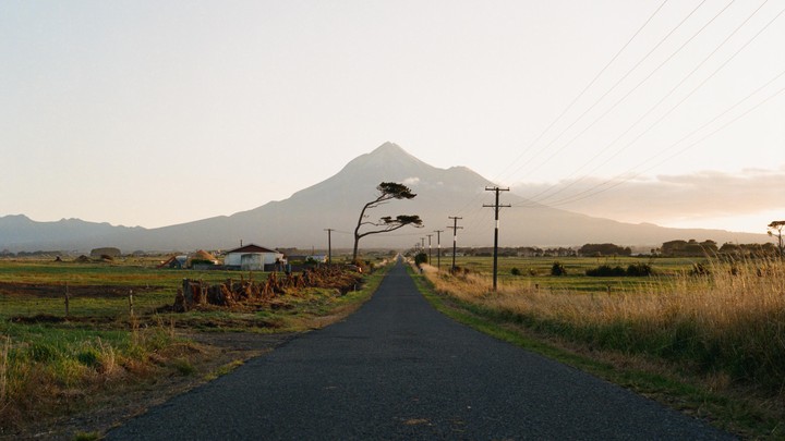 A long, straight road leads towards a large mountain under a hazy sky.