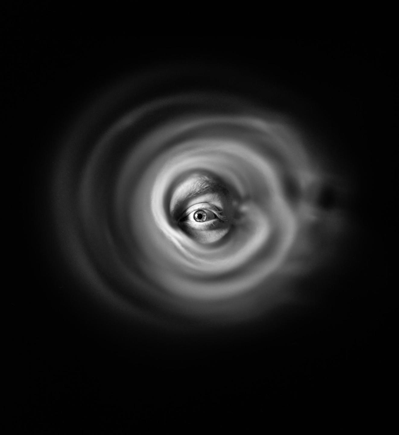 A single eye is visible through a swirling, circular pattern of light and shadow.
