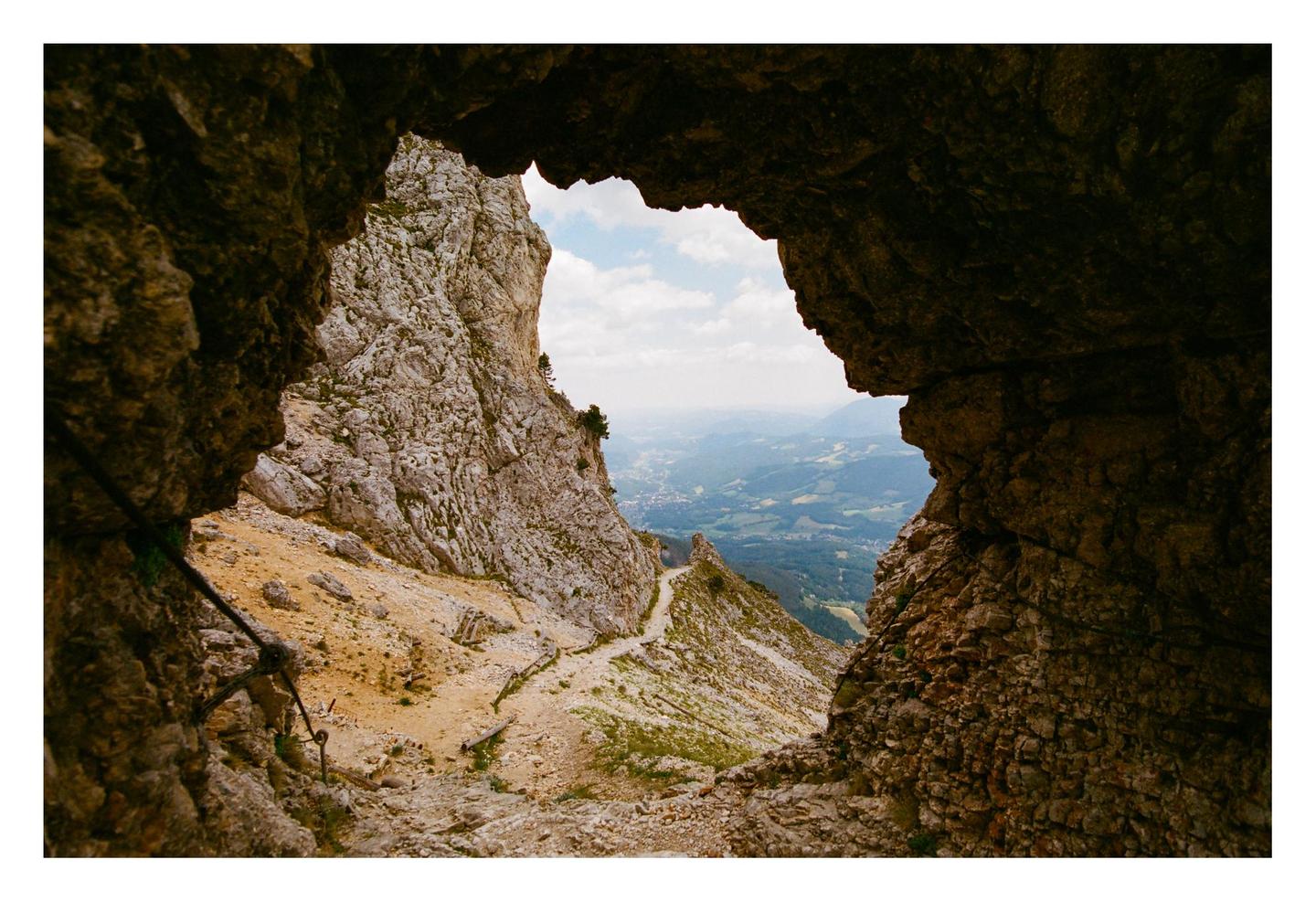 A view of a mountain path and valley is framed by a rock formation.